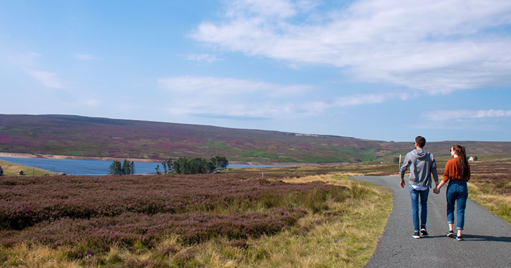 Couple walking in Durham Dales, reservoir and heather in view